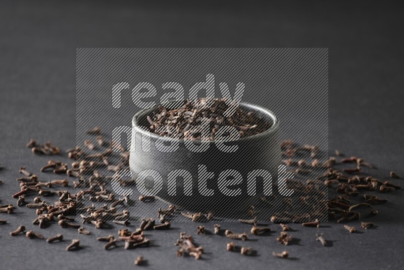 A black pottery bowl full of cloves on a black flooring