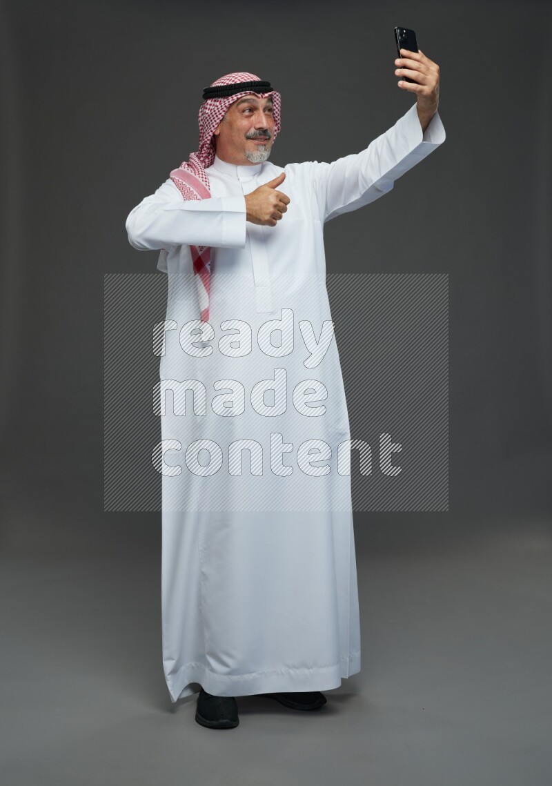Saudi man with shomag Standing taking selfie on gray background