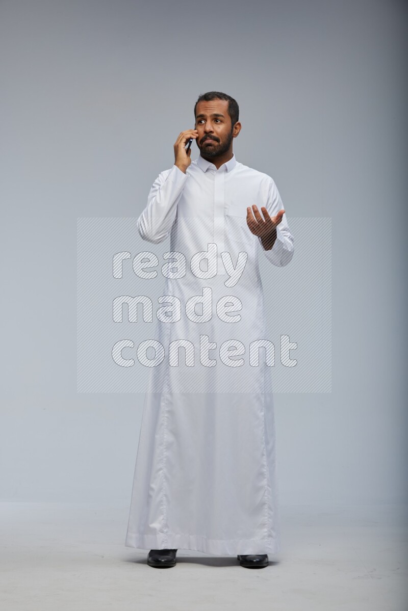 Saudi man wearing Thob standing talking on phone on Gray background