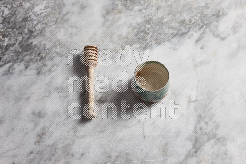 Multicolored pottery bowl with wooden honey dipper on the side on grey marble background