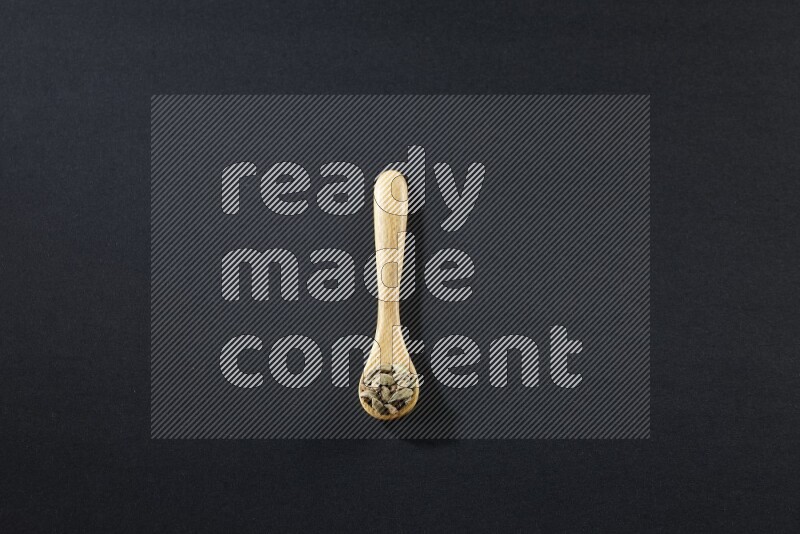 A wooden spoon full of cardamom on black flooring