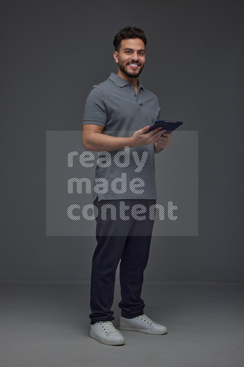 A man wearing casual standing and using his tablet and making multi hand gestures different angles eye level on a gray background