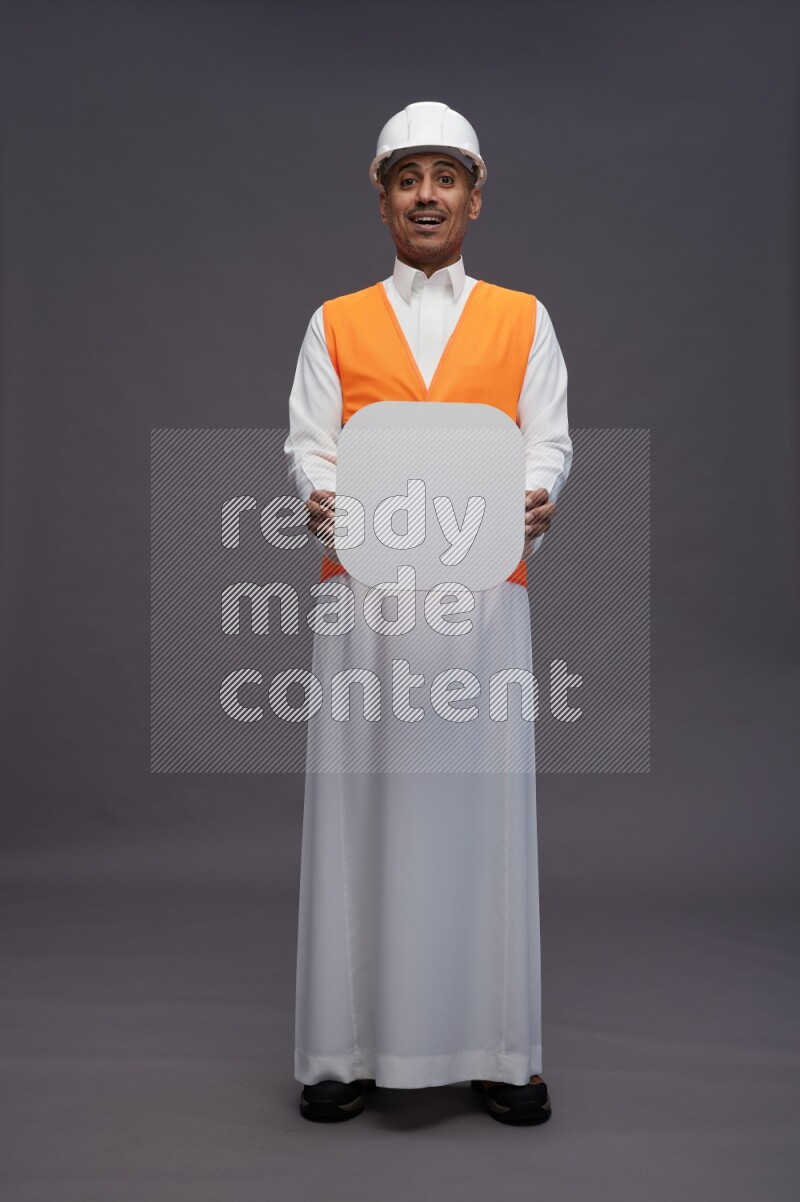Saudi man wearing thob with engineer vest standing holding social media sign on gray background
