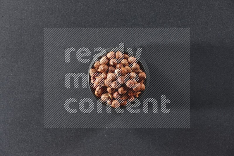 A black pottery bowl full of peeled hazelnuts on a black background in different angles