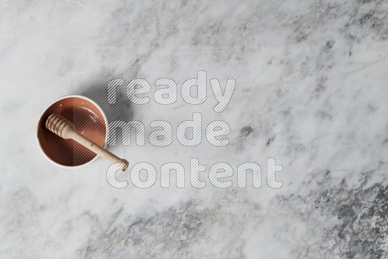 Multicolored pottery bowl with wooden honey dipper in it on grey marble background