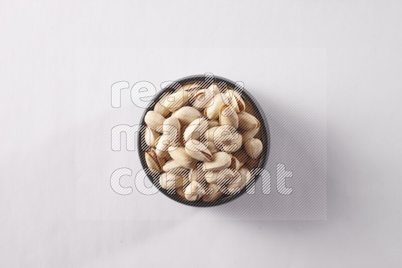 Pistachios in a black pottery bowl on white background