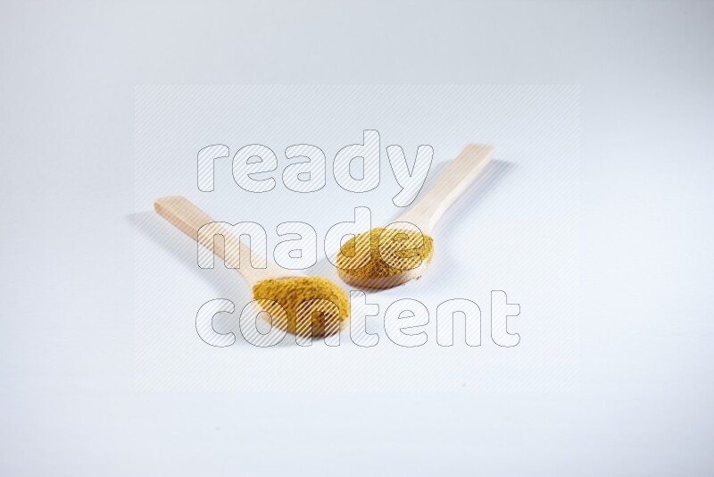 ملعقتان خشبيتان ممتلئتان ببودرة الكركم على خلفية بيضاء