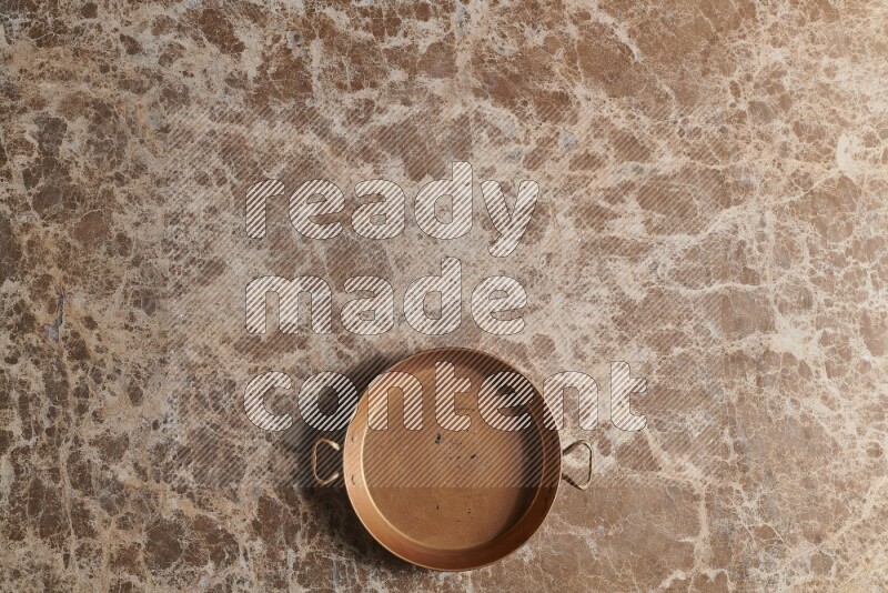 A small copper pan on beige marble background