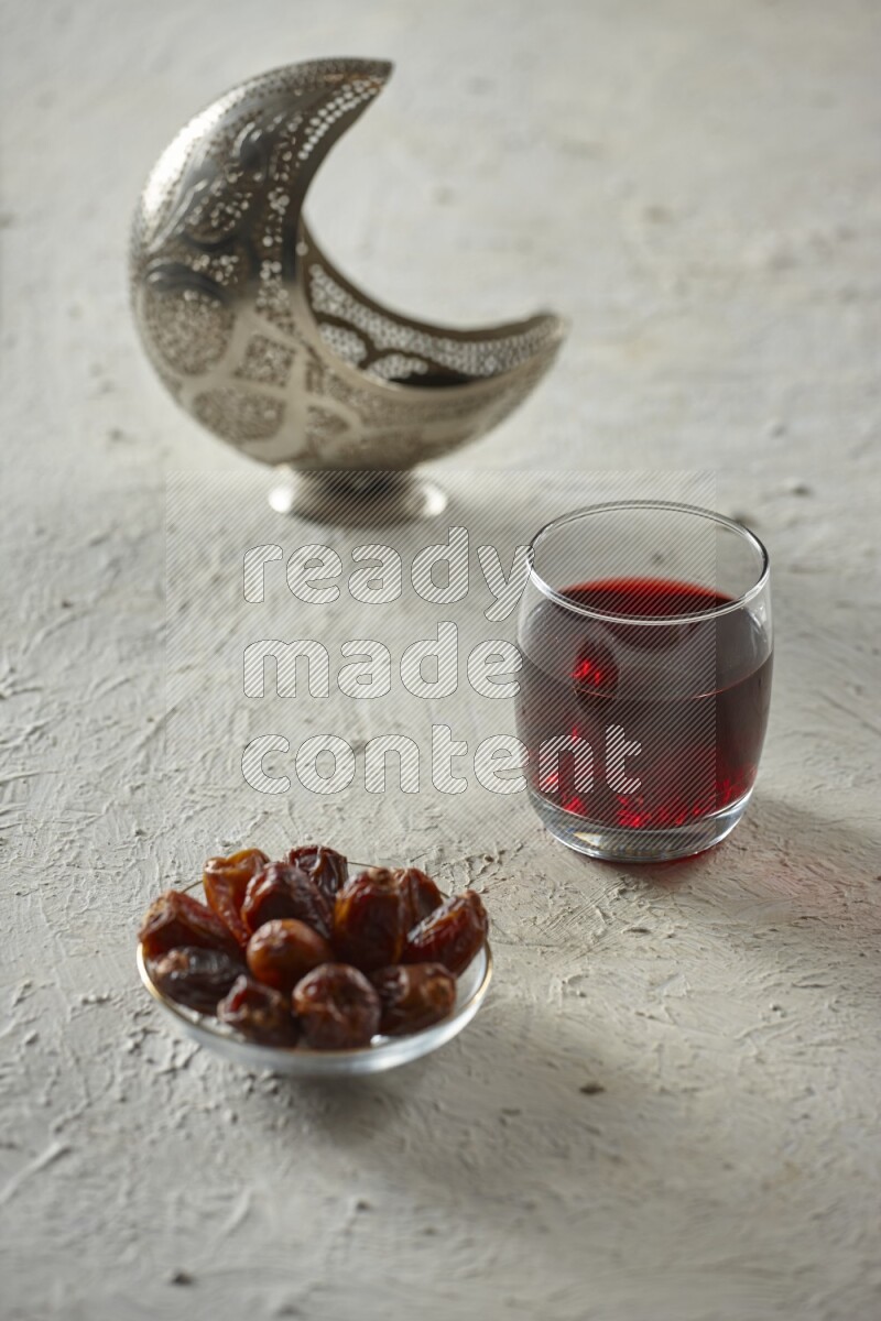 A silver lantern with different drinks, dates, nuts, prayer beads and quran on textured white background