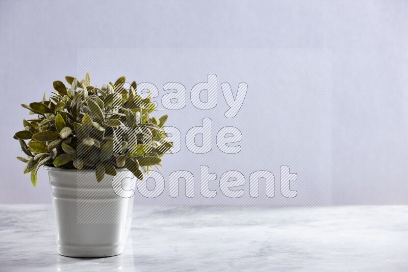 Multiple green artificial plants in white pot on grey marble background
