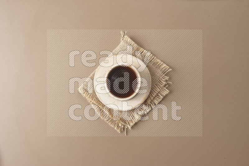 A beige pottery cup of coffee surrounded by roasted coffee beans on beige background