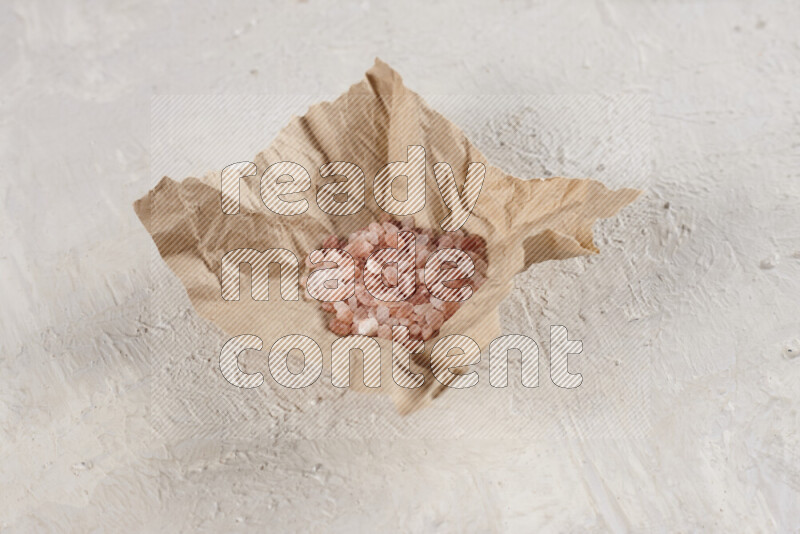 A crumpled piece of paper full of pink himalayan salt on white background