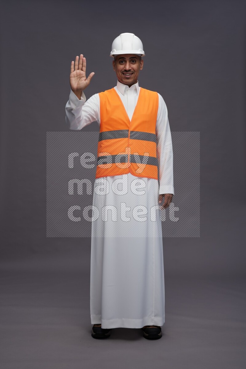 Saudi man wearing thob with engineer vest standing interacting with the camera on gray background