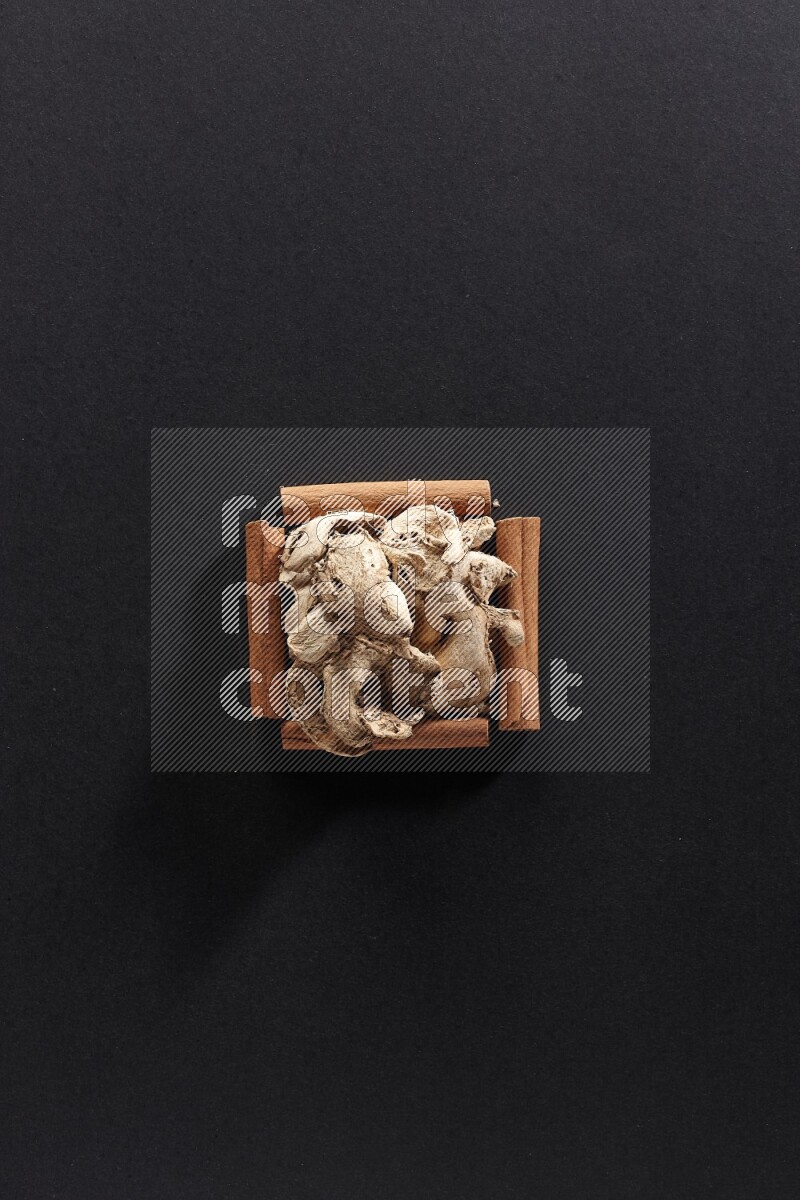 A single square of cinnamon sticks full of dried ginger on black flooring