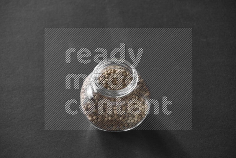 A glass spice jar full of white peppers on black flooring
