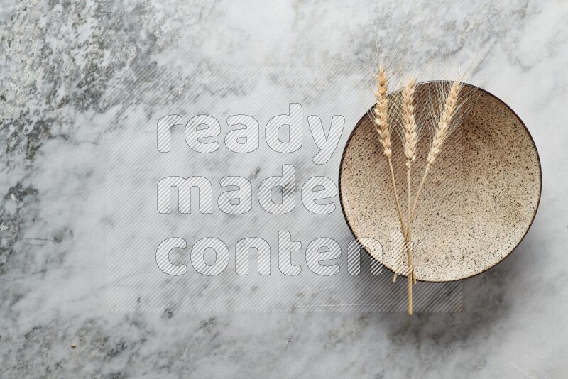 Wheat stalks on multicolored pottery plate on grey marble background