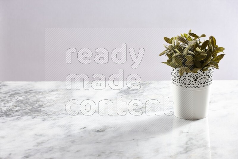 Green artificial plant in white decorative pot on grey marble background