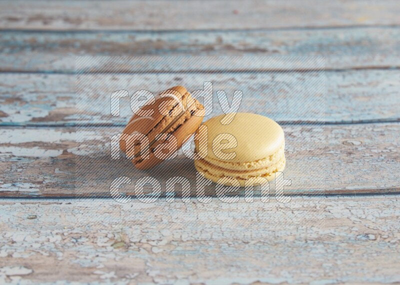 45º Shot of of two assorted Brown Irish Cream, and Yellow Vanilla macarons on light blue background