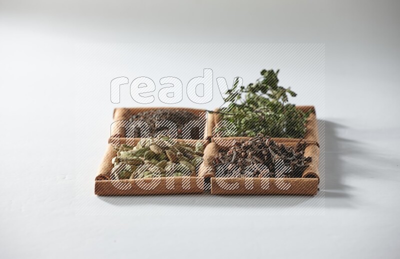 4 مربعات من أعواد القرفة ممتلئة بالشاي والهيل والنعناع والقرنفل على أرضية بيضاء