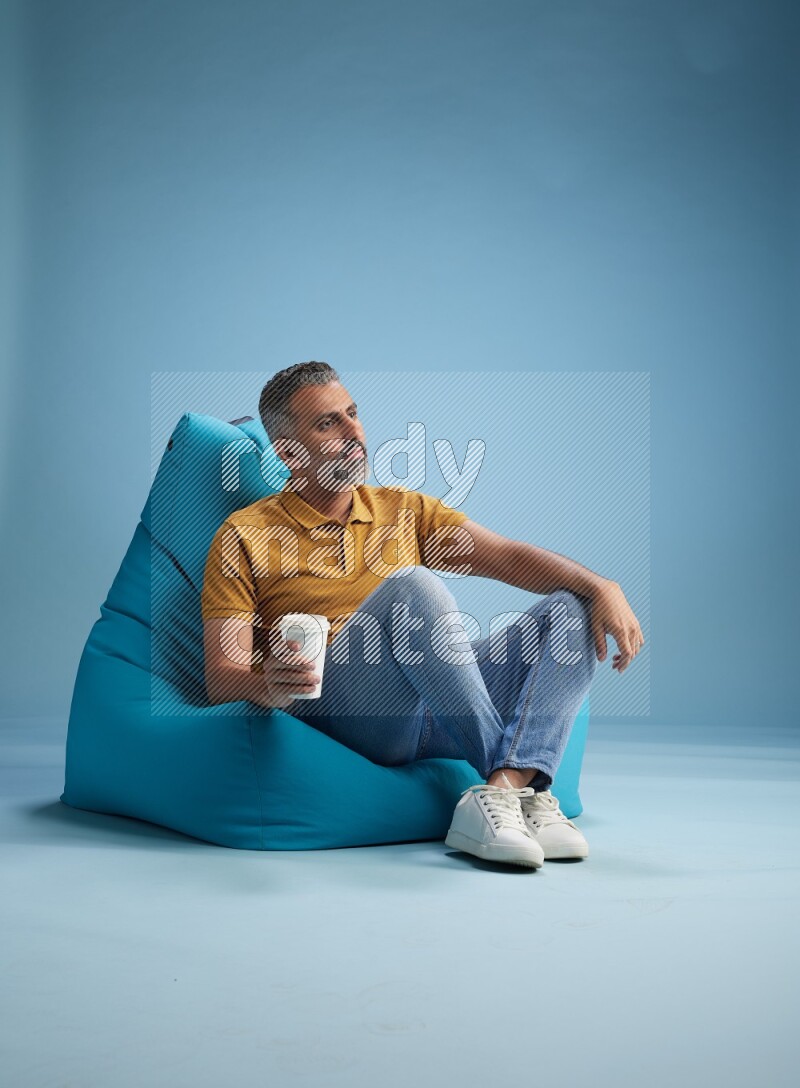 A man sitting on a blue beanbag and drinking coffee