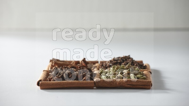 4 مربعات من أعواد القرفة ممتلئة بالهيل واليانسون النجمي والقرنفل والقرفة على أرضية بيضاء