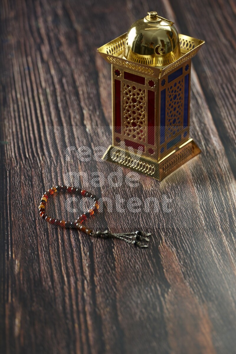 A golden lantern with different drinks, dates, nuts, prayer beads and quran on brown wooden background