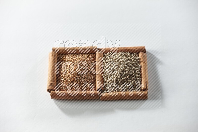 مربعان من أعواد القرفة ممتلئان بحبوب الخردل وحبوب الفلفل الأبيض علي خلفية بيضاء