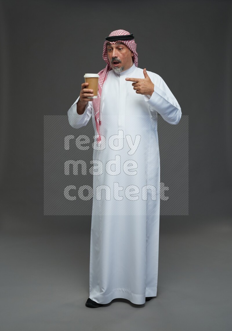Saudi man with shomag Standing holding paper cup on gray background