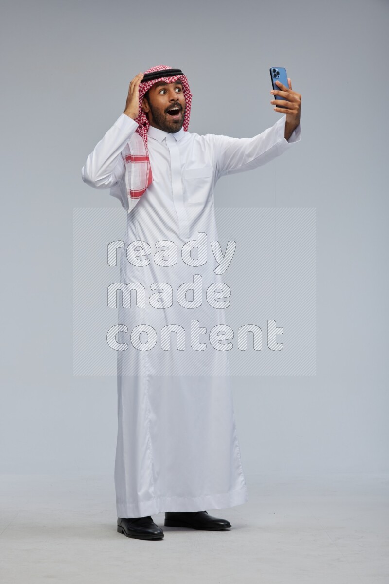 Saudi man Wearing Thob and shomag standing taking selfie on Gray background