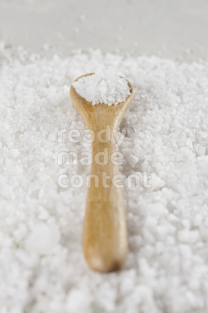 A wooden spoon full of white salt on white background