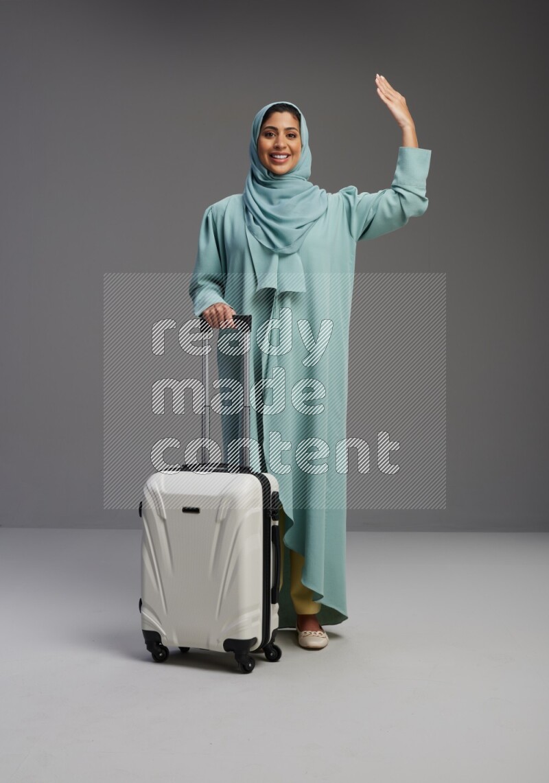 Saudi Woman wearing Abaya standing holding Travel bag on Gray background