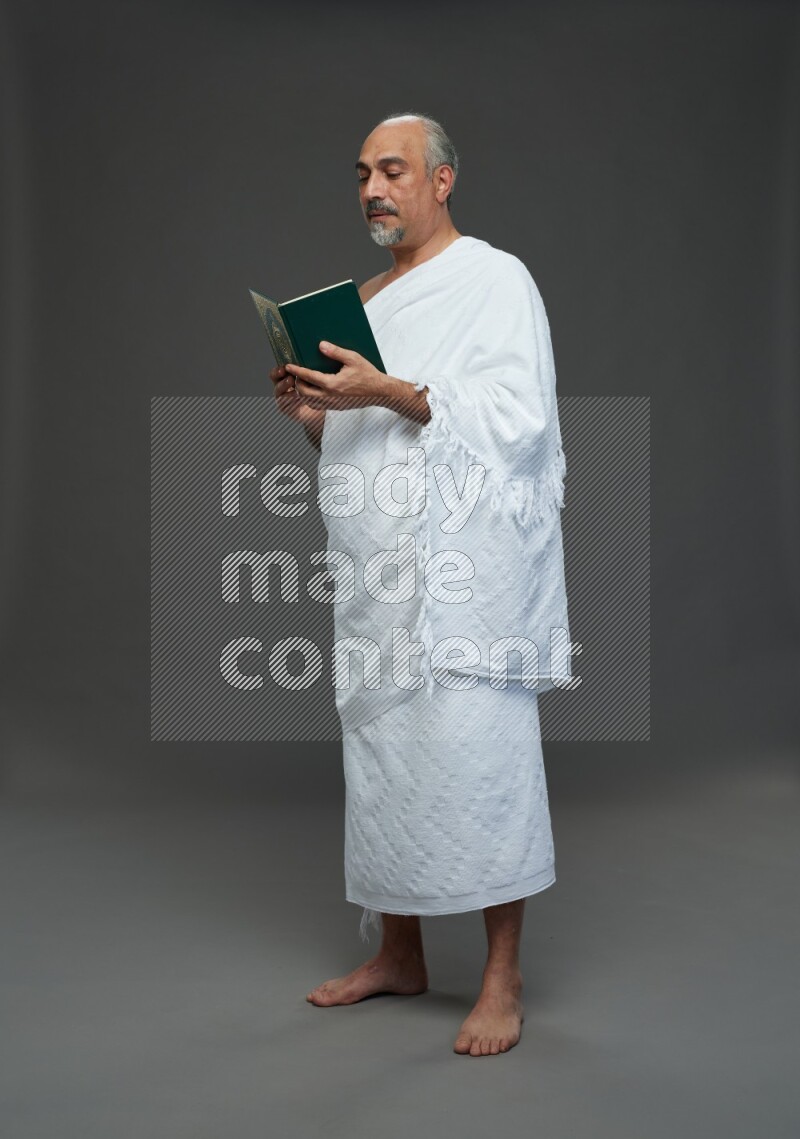 A man wearing Ehram Standing reading quran on gray background