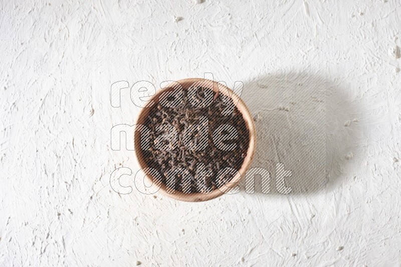 A wooden bowl full of cloves on a white flooring