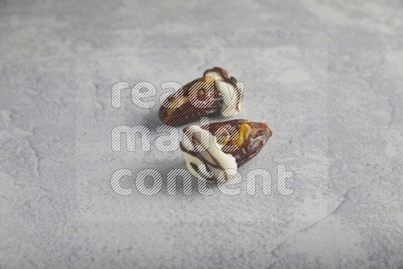 two pistachio stuffed dates covered with white chocolate with dark chocolate drizzle on a light grey background