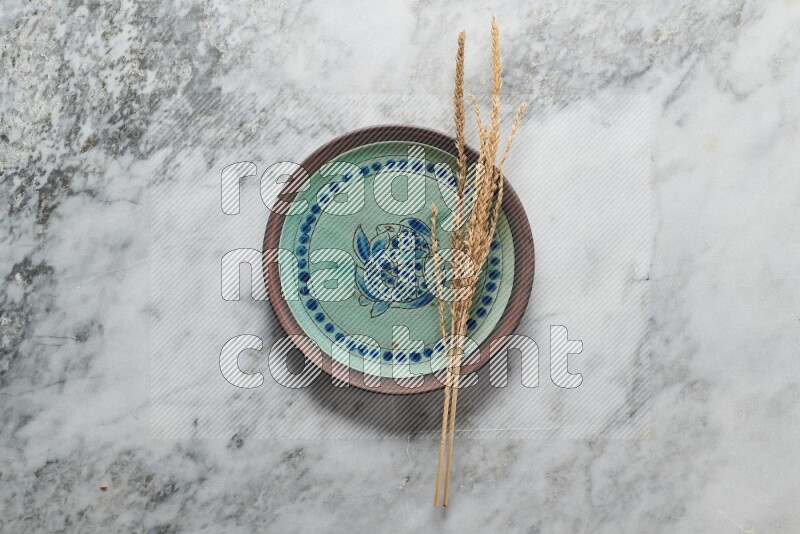 Wheat stalks on decorative pottery plate on grey marble background