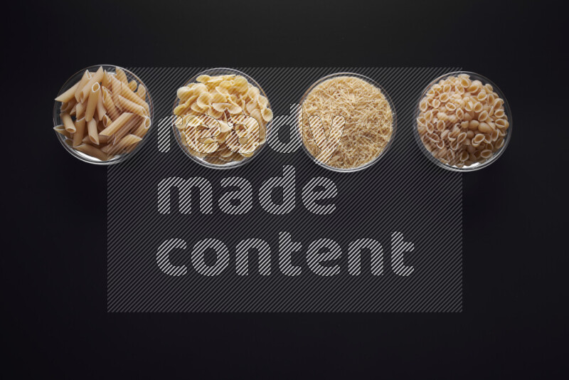 Different pasta types in glass bowls on black background