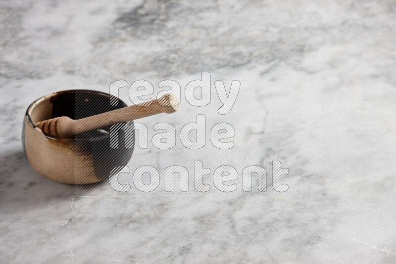 Multicolored pottery bowl with wooden honey dipper in it on grey marble background