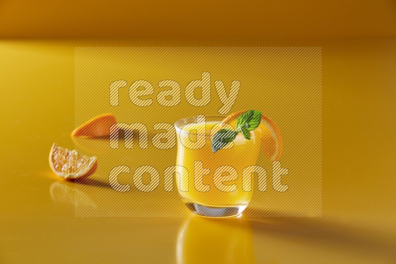 glass of orange juice with orange & mint  on yellow background