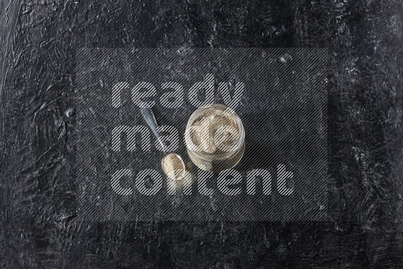 وعاء زجاجي وملعقة معدنية ممتلئان ببودرة الفلفل الأبيض على أرضية سوداء