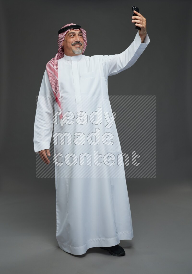 Saudi man with shomag Standing taking selfie on gray background