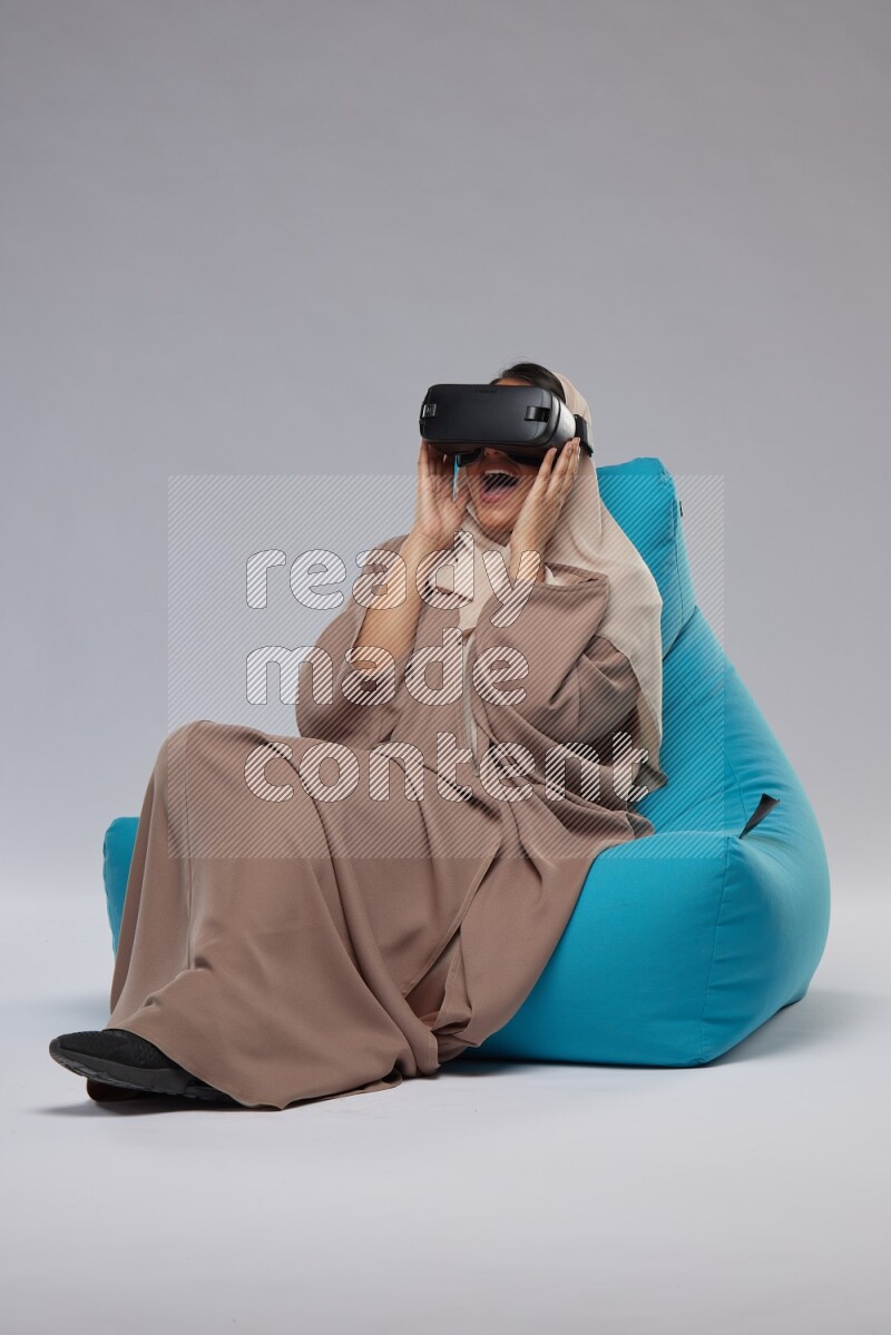 A Saudi woman sitting on a blue beanbag and gaming with VR