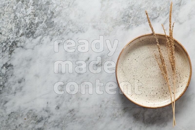 Wheat stalks on multicolored pottery plate on grey marble background