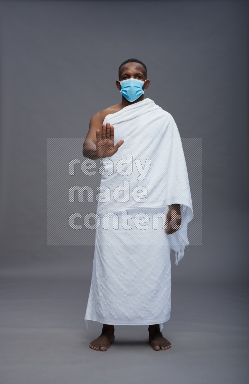 A man wearing Ehram with face mask Standing Interacting with the camera on gray background