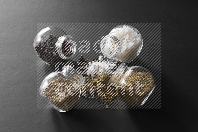 ملح وفلفل أسود وفلفل أبيض وكمون في أوعية زجاجية علي خلفية سوداء