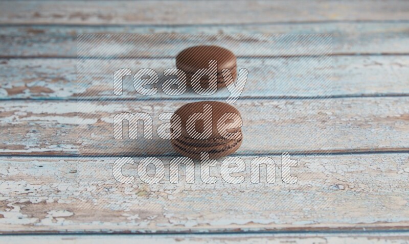 45º Shot of two Brown Dark Chocolate macarons on light blue wooden background