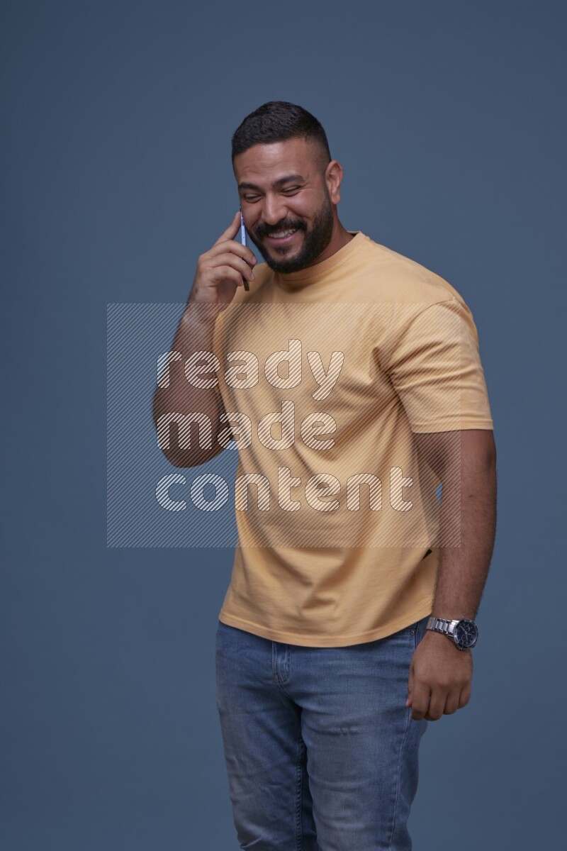 رجل يرتدي بنطال ازرق جينز وقميص اصفر بأكمام قصيره يتحدث بجواله
