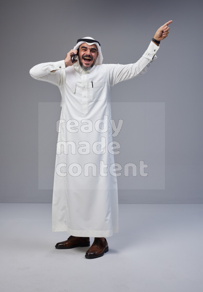 Saudi man Wearing Thob and white Shomag standing talking on phone on Gray background