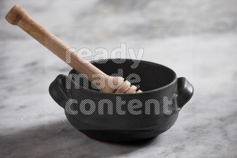 Black pottery bowl with wooden honey dipper in it on grey marble background