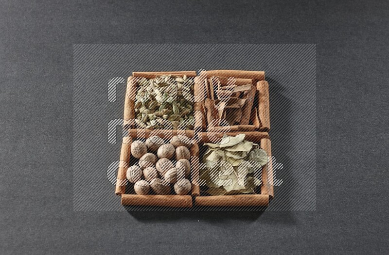 4 مربعات من عيدان القرفة ممتلئة بقطع القرفة وحبوب الهيل وأوراق الغار وجوزة الطيب على أرضية سوداء