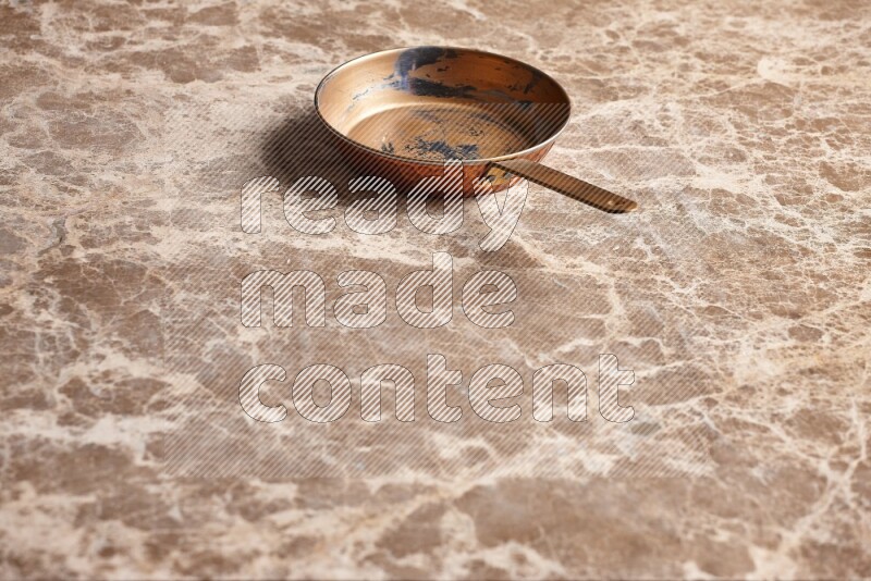 A small copper pan on beige marble background